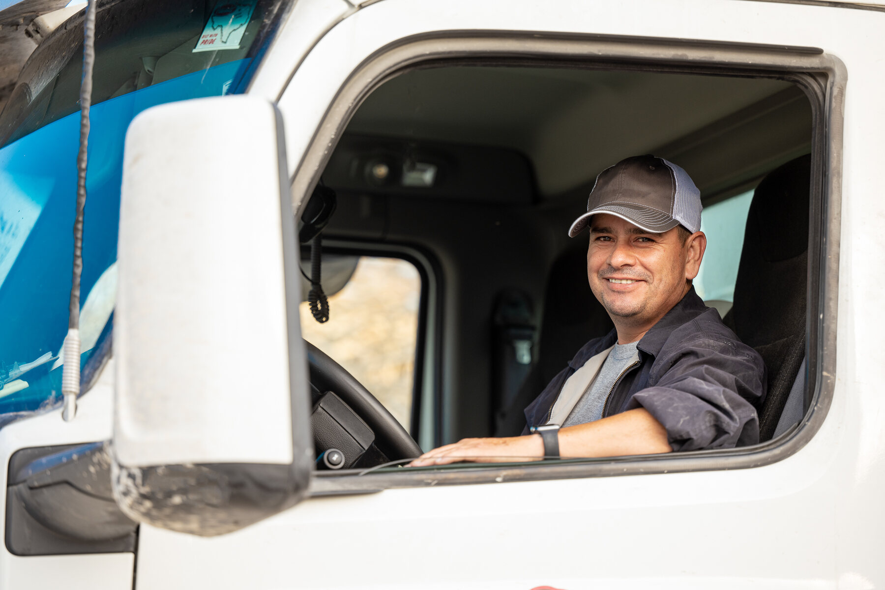 A hauler smiling from the cab window of a dump truck